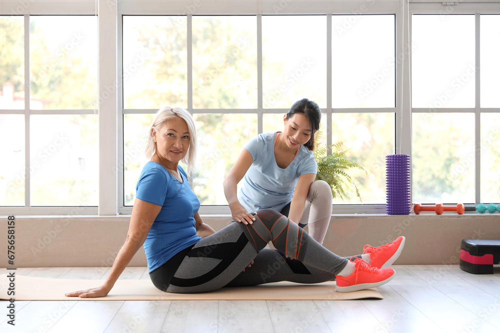 Mature woman training with therapist on mat in rehabilitation center