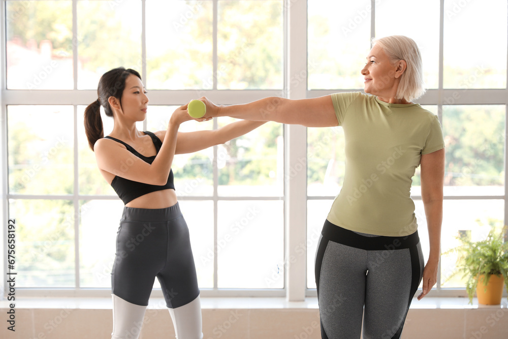 Mature woman training with dumbbell and therapist in rehabilitation center