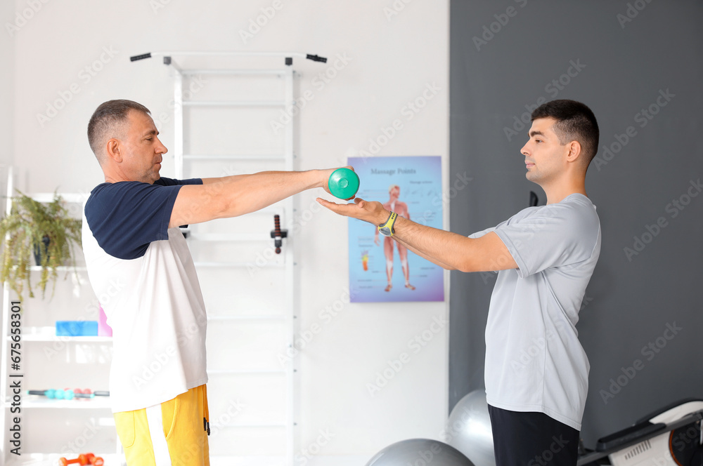 Mature man training with dumbbells and therapist in rehabilitation center