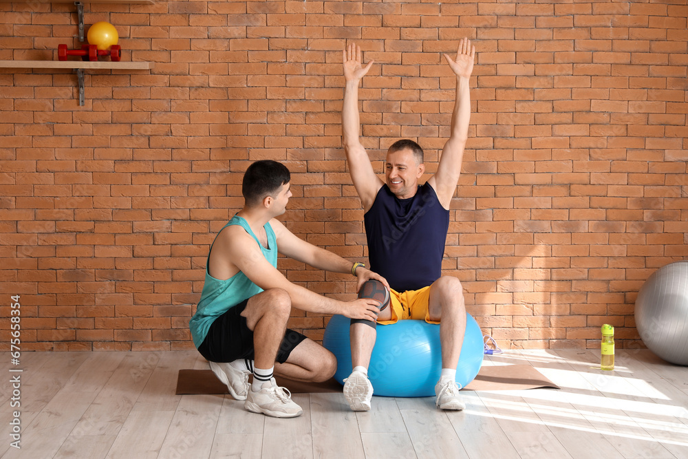 Mature man training on fitball with therapist in rehabilitation center