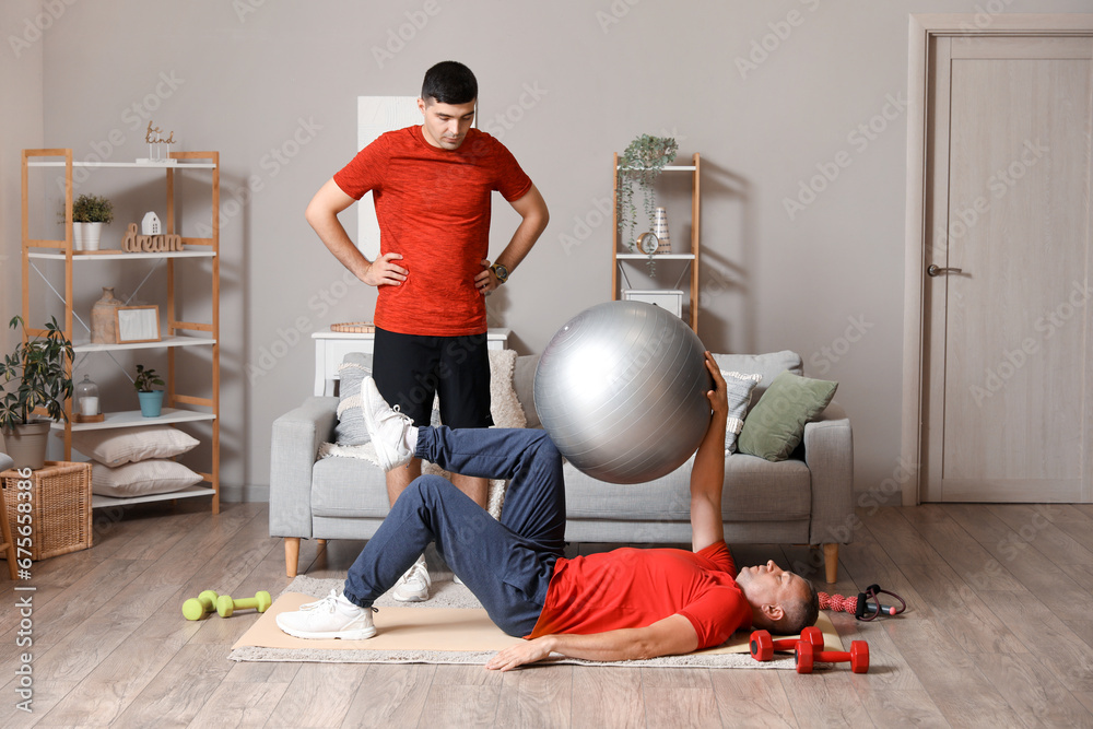 Mature man training with fitball and rehabilitation therapist at home