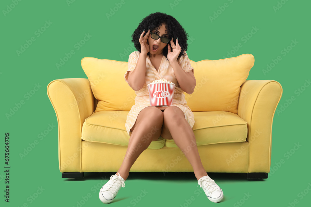 Shocked beautiful woman in 3D glasses with popcorn watching movie on sofa against green background