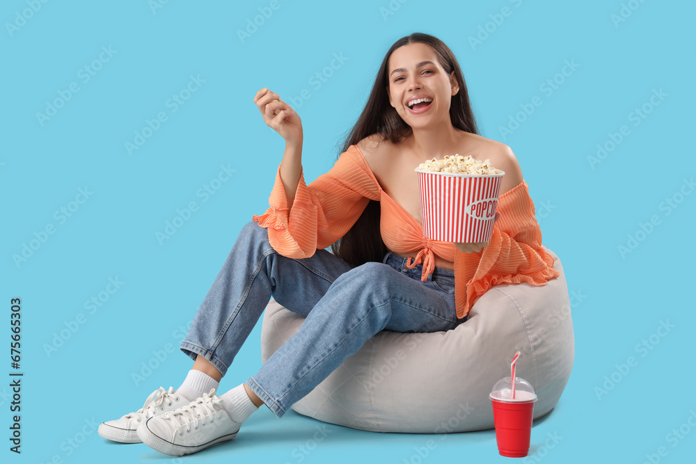 Young woman with popcorn watching movie on beanbag against blue background