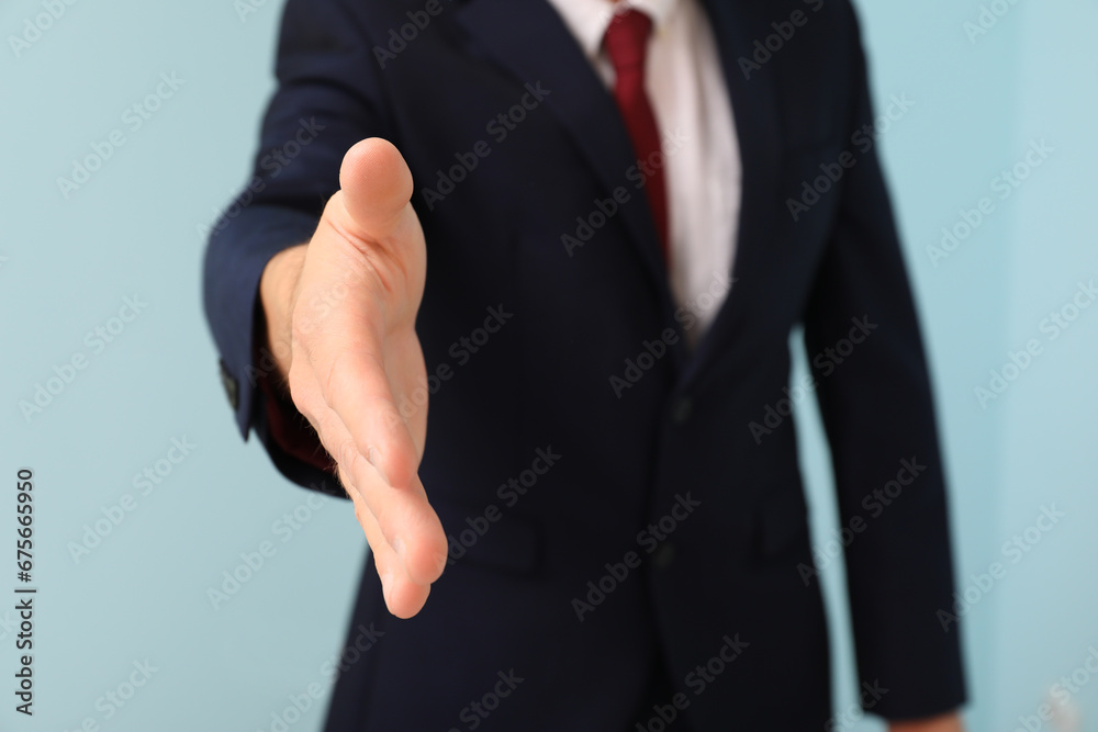 Businessman reaching out for handshake on blue background, closeup