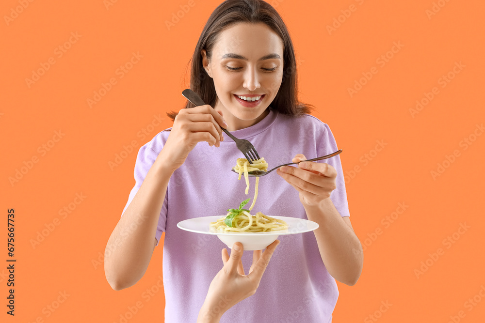 Young woman eating tasty pasta on orange background