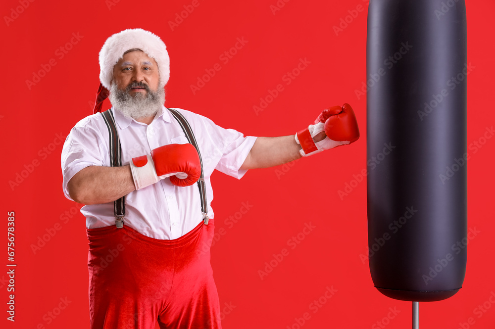 Sporty Santa Claus with boxing gloves punching bag on red background