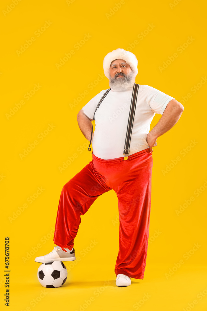 Sporty Santa Claus with soccer ball on yellow background