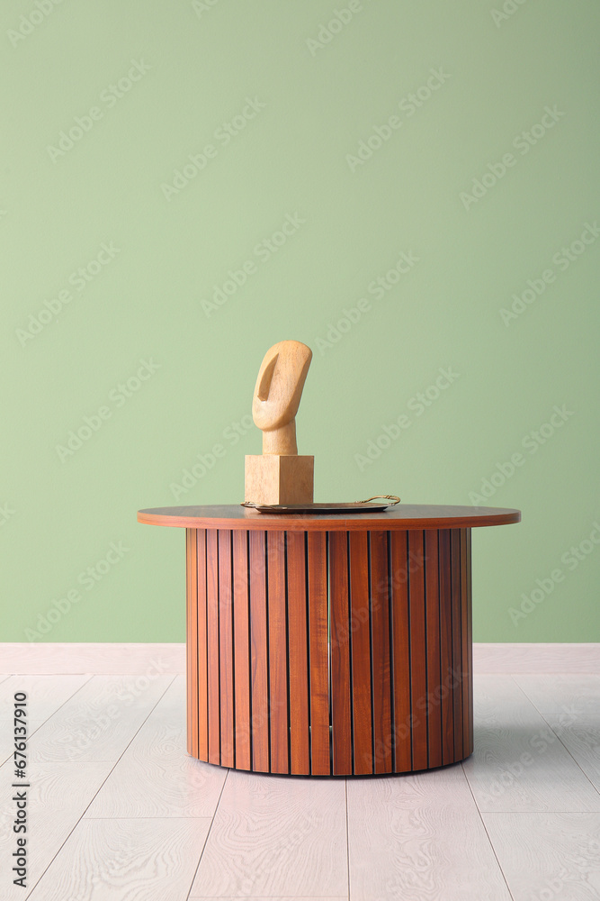 Coffee table with wooden figurine and tray near green wall