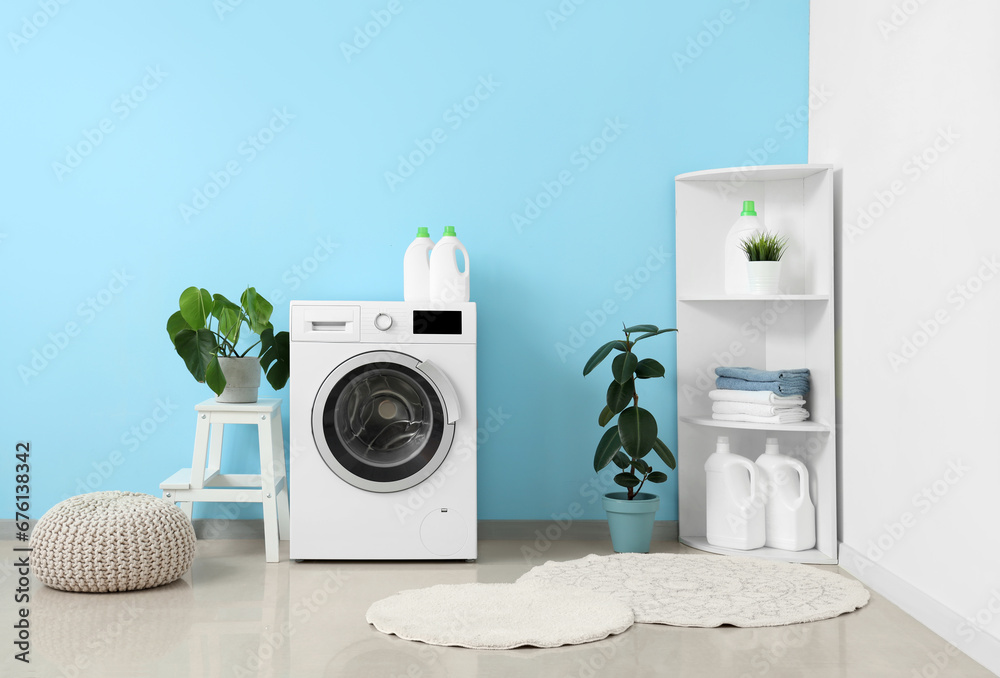 Washing machine, shelving unit, houseplants and pouf near blue wall