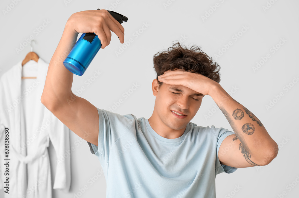 Handsome young man with tattoo applying hair spray on his curly hair in bathroom