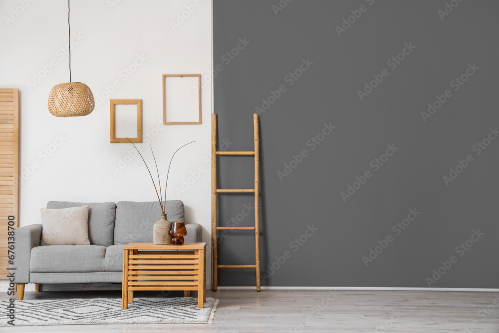 Interior of light living room with grey sofa and branches in vase on wooden table