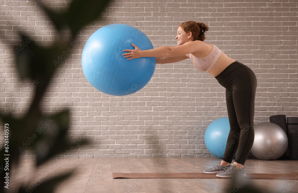 Beautiful young woman in sportswear exercising with fitness ball at gym