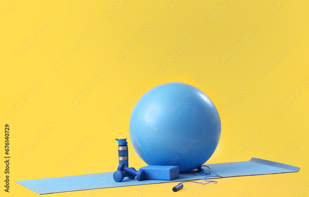 Fitness ball, yoga mat and sports equipment on yellow background