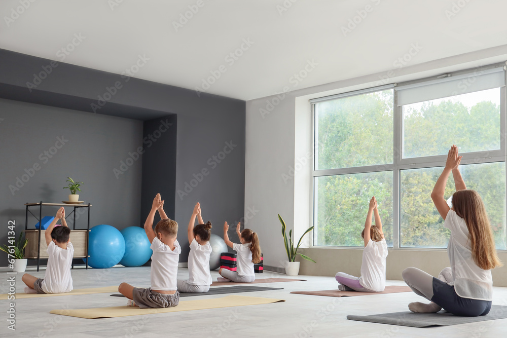 Female yoga instructor with group of little children in gym