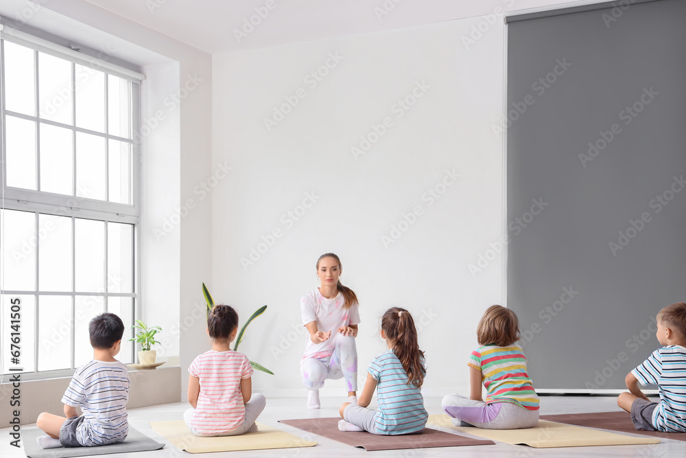 Group of little children practicing yoga with instructor in gym