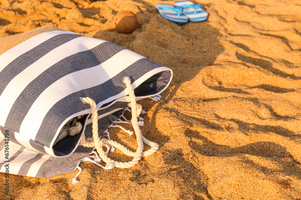 Stylish beach bag and towel on sand