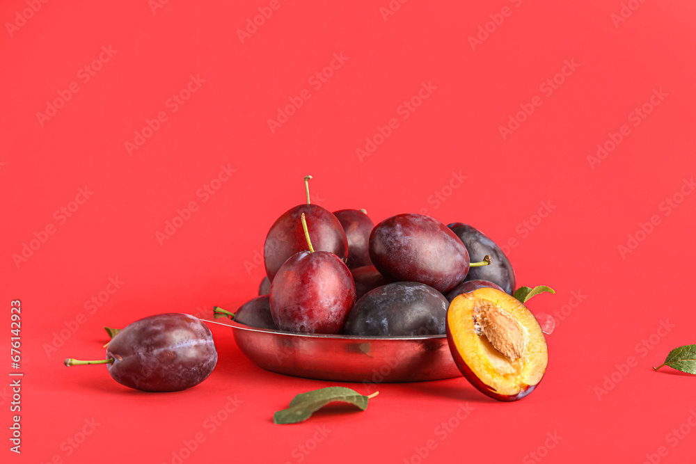 Metal plate with fresh ripe plums on red background