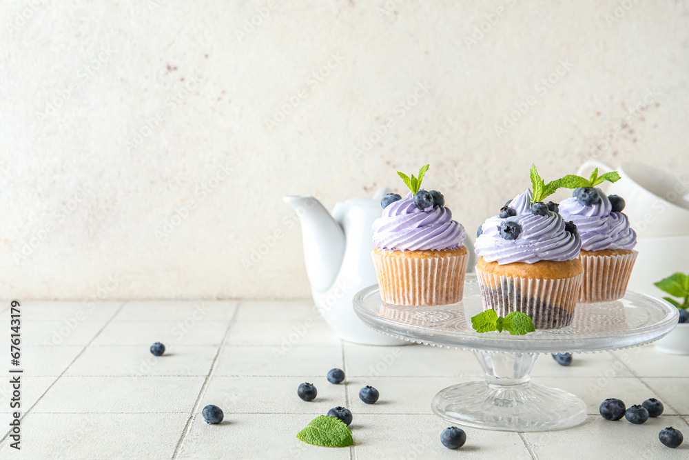 Glass stand of delicious cupcakes with blueberries and mint on white tile table