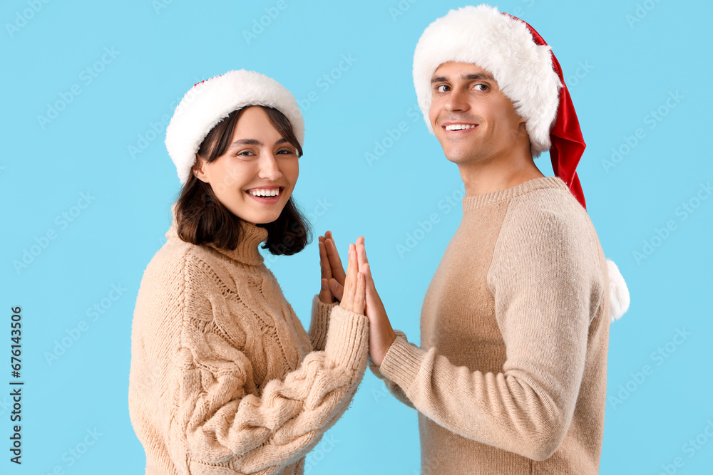 Happy young couple in Santa hats on blue background