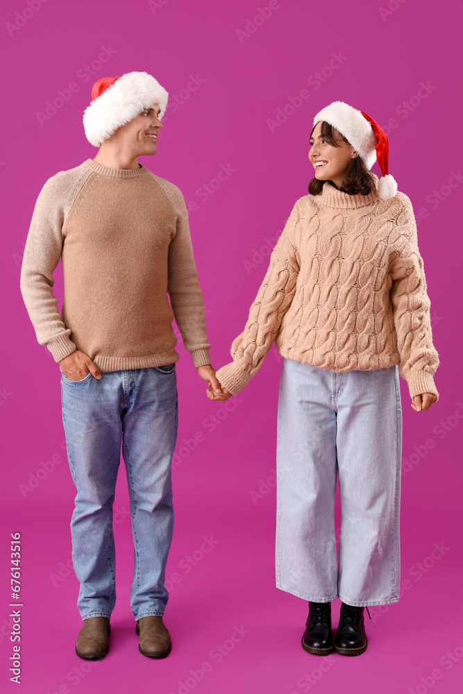 Happy young couple in Santa hats on purple background