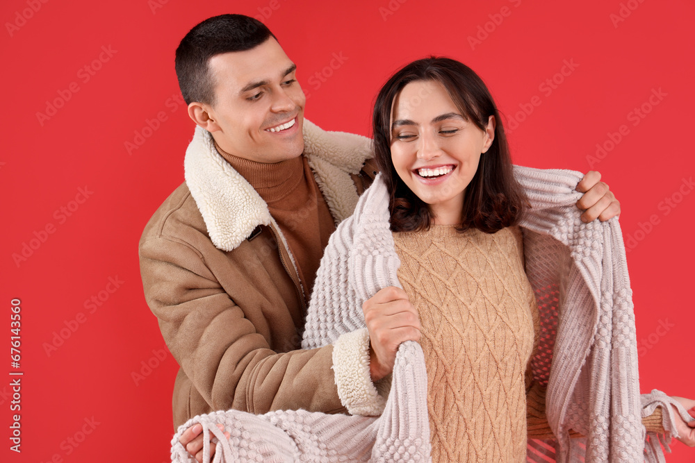 Happy young couple with plaid on red background