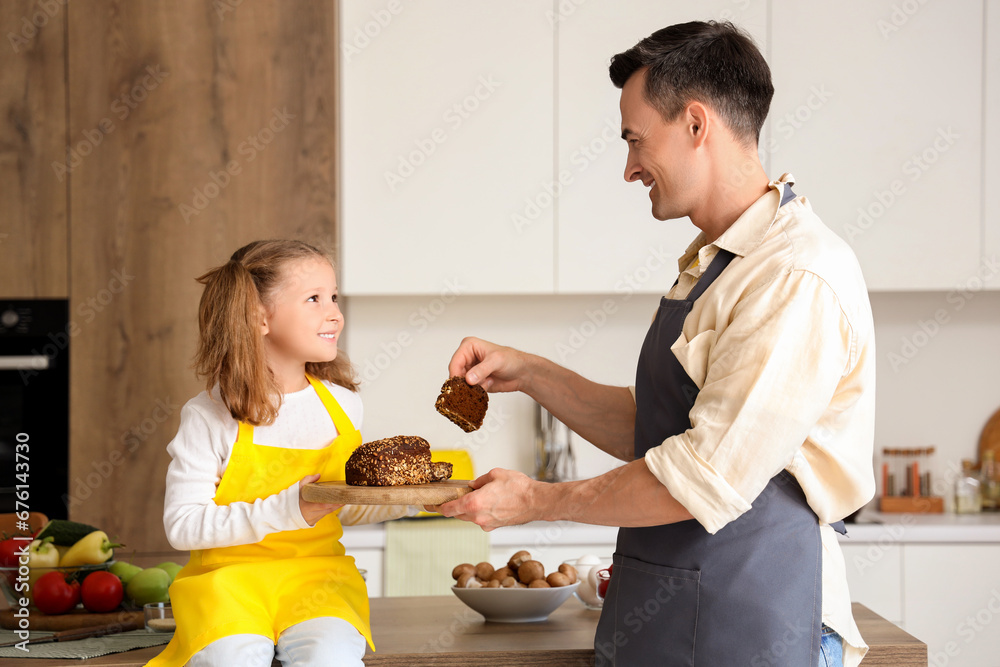 Cute little girl with bread and her dad in kitchen