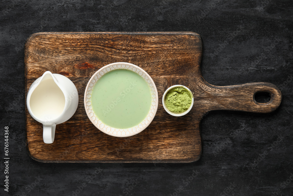 Wooden board with fresh matcha tea, powder and milk on dark background