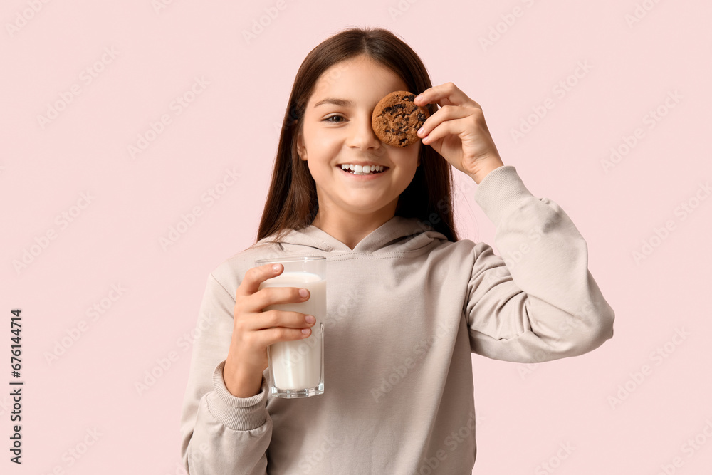 Happy little girl holding sweet chocolate cookie and glass of fresh milk on pink background