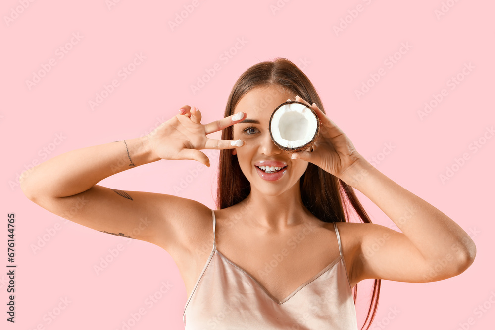 Beautiful young woman with coconut and oil showing victory gesture on pink background