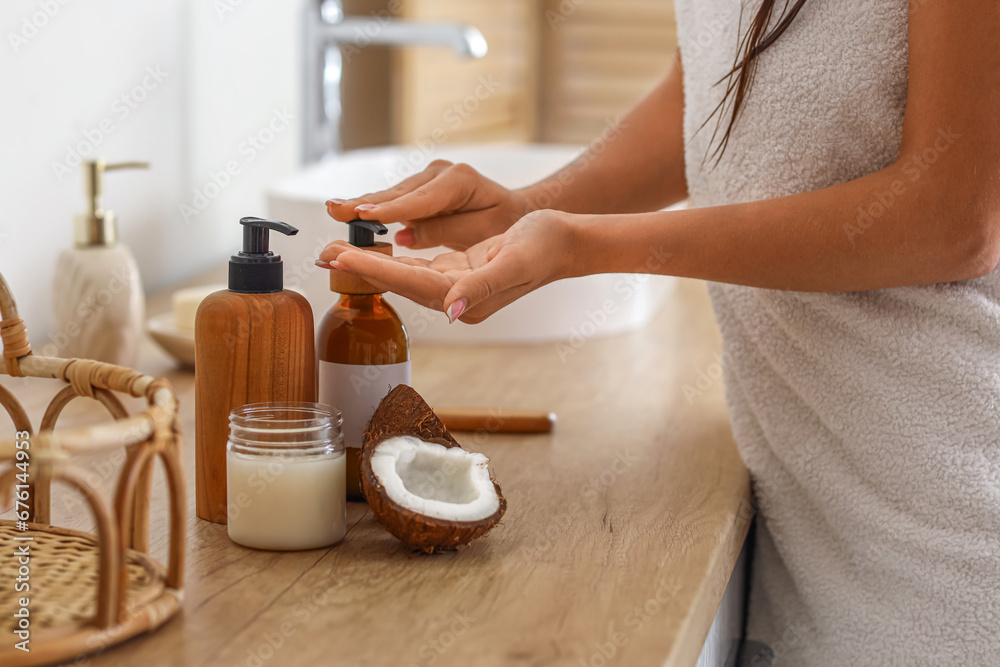 Beautiful young woman applying coconut oil in bathroom, closeup