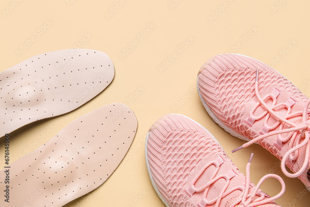 Pair of stylish pink sneakers with orthopedic insoles on beige background