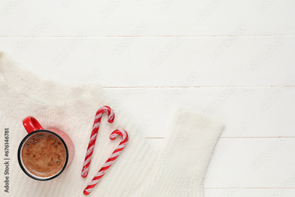 Mug of coffee with candy canes and sweater on white wooden background