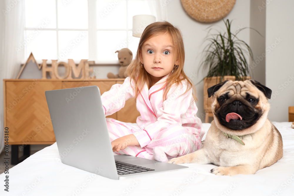 Little girl with cute pug dog and laptop in bedroom