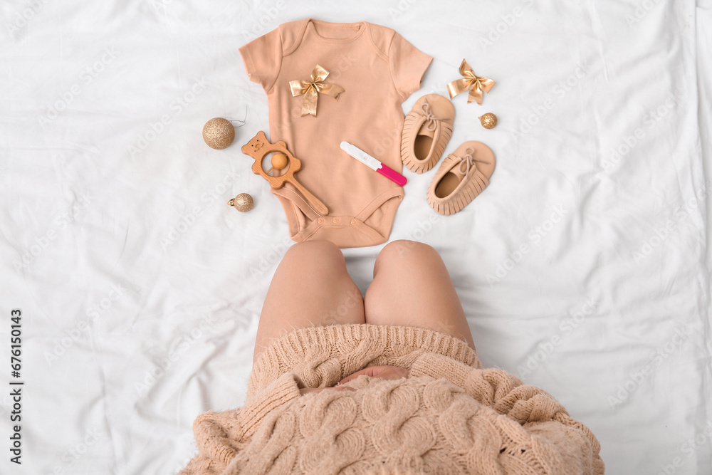 Pregnant woman with baby accessories, test and Christmas decorations on bed