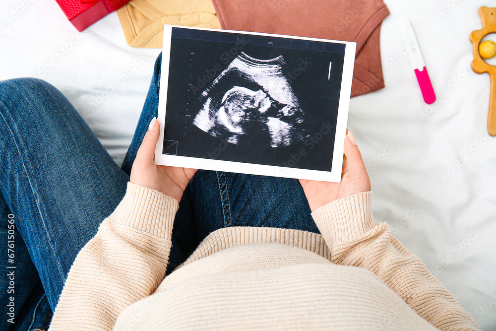 Pregnant woman with sonogram image on bed, closeup