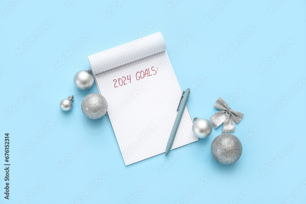 Notebook with text 2024 GOALS, pen and silver Christmas balls on blue background