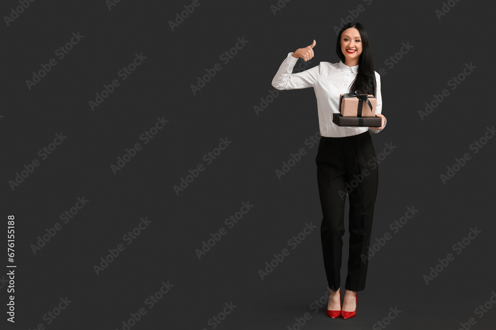 Beautiful stylish woman with gift boxes showing thumb-up gesture on dark background. Black Friday Sale