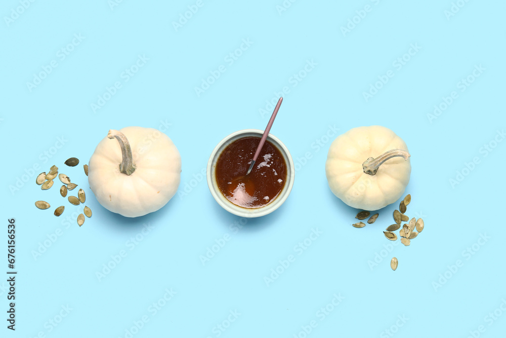 Bowl of sweet pumpkin jam and seeds on blue background