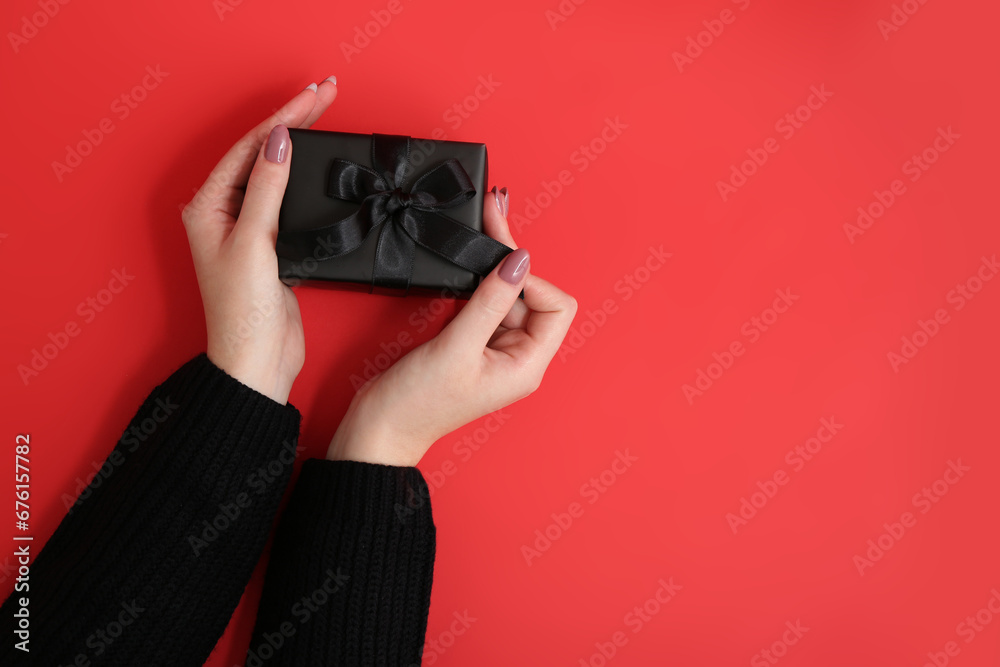 Female hands with gift box on red background. Black Friday