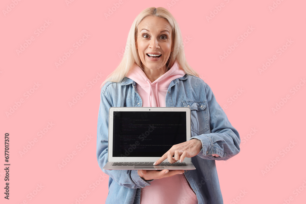 Mature female programmer with laptop on pink background