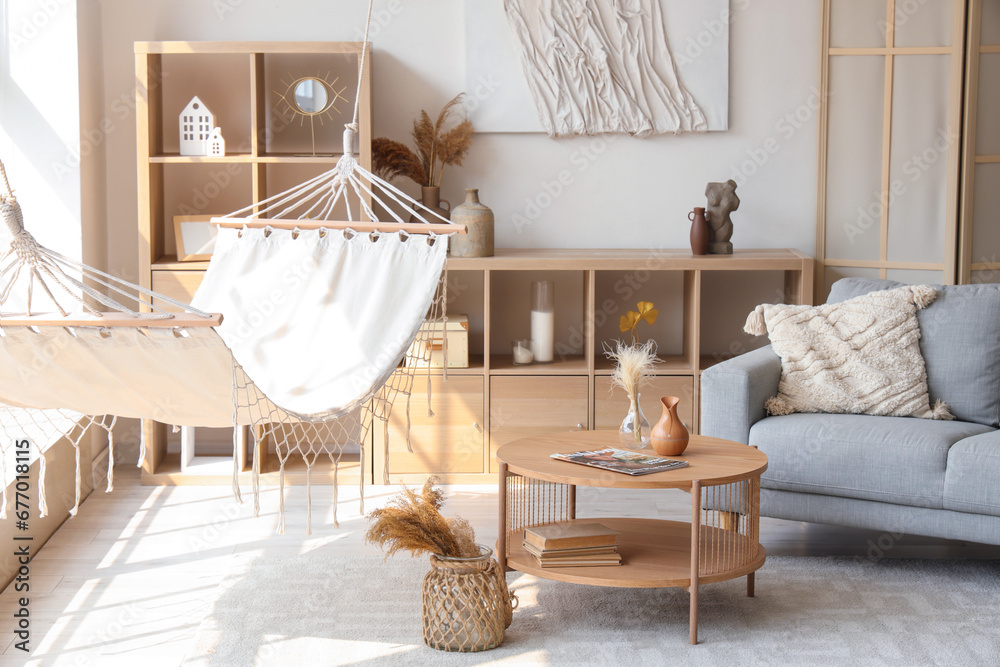 Interior of light living room with hammock, table and sofa