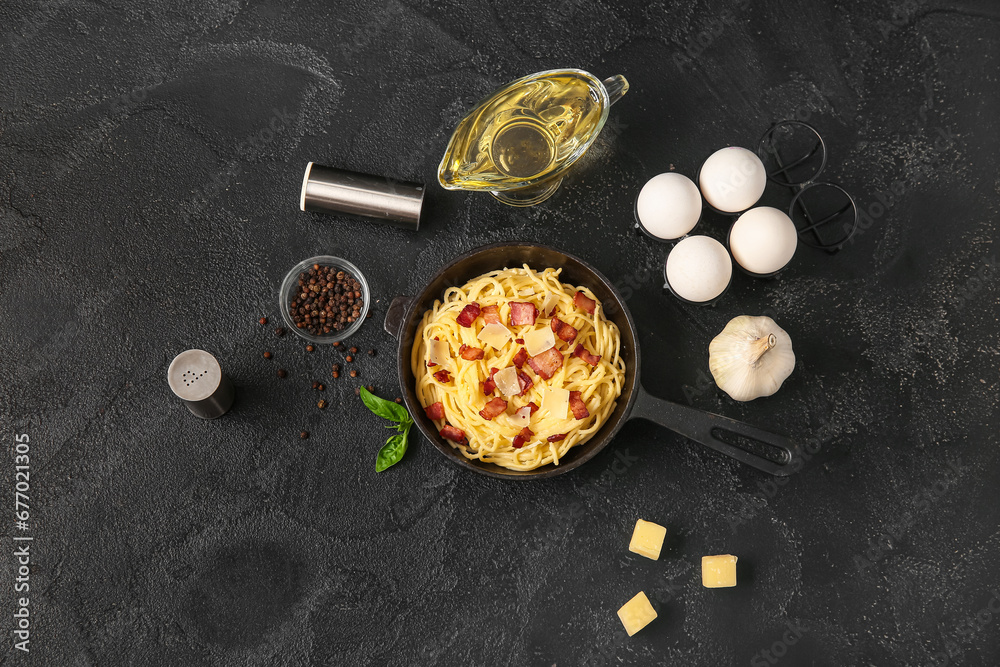 Frying pan with tasty pasta carbonara and ingredients on black background