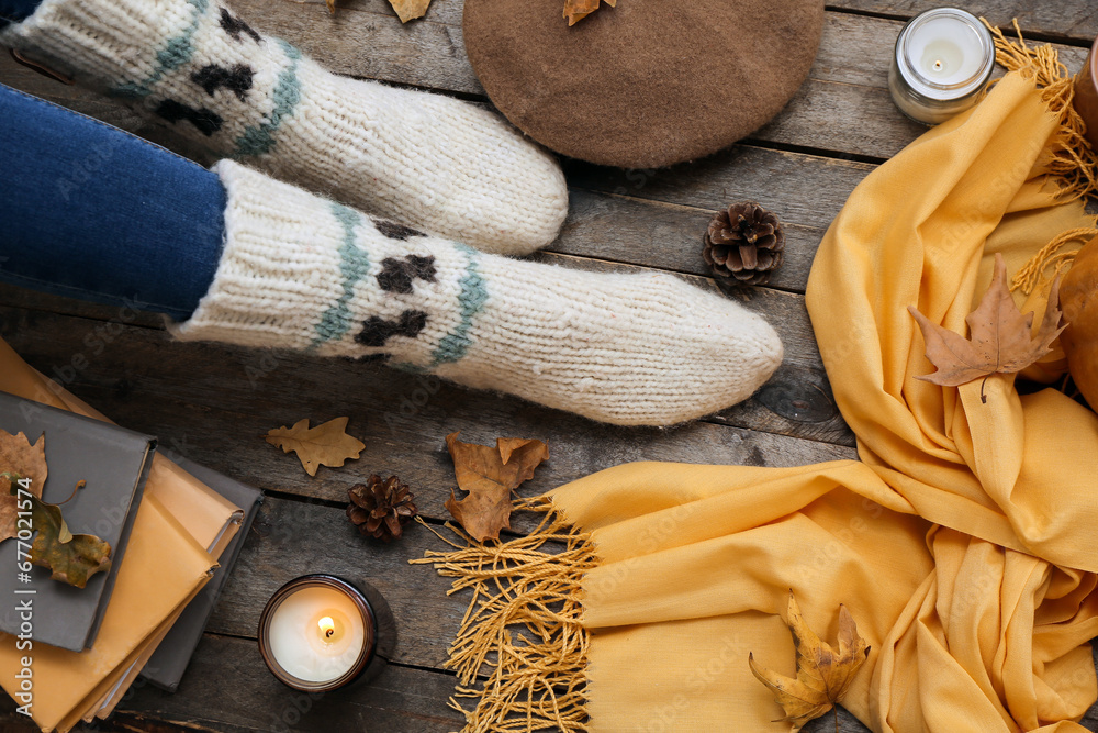 Female legs in warm socks, accessories and fallen leaves on wooden background, closeup