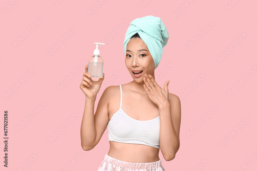 Surprised young Asian woman with shower gel on pink background