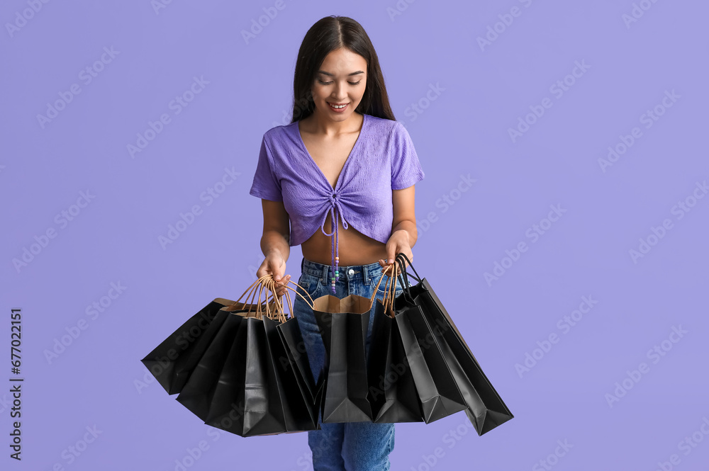 Beautiful young Asian woman with shopping bags on purple background. Black Friday sale