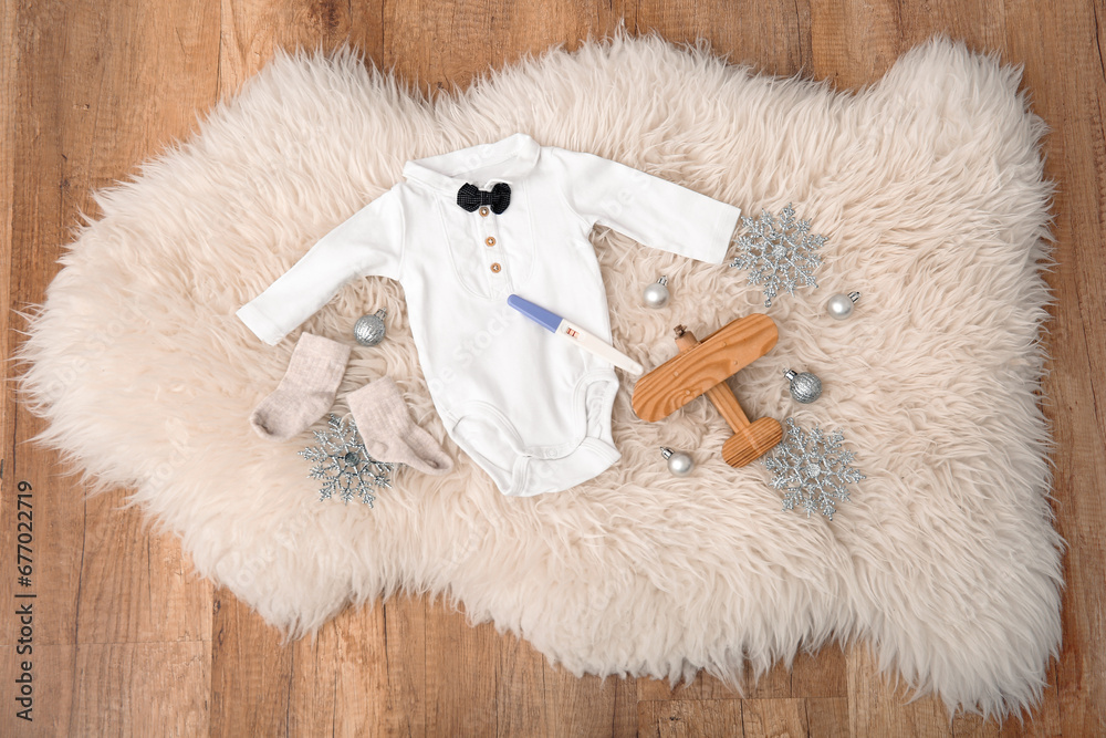 Composition with stylish baby clothes, positive pregnancy test and Christmas decorations on floor