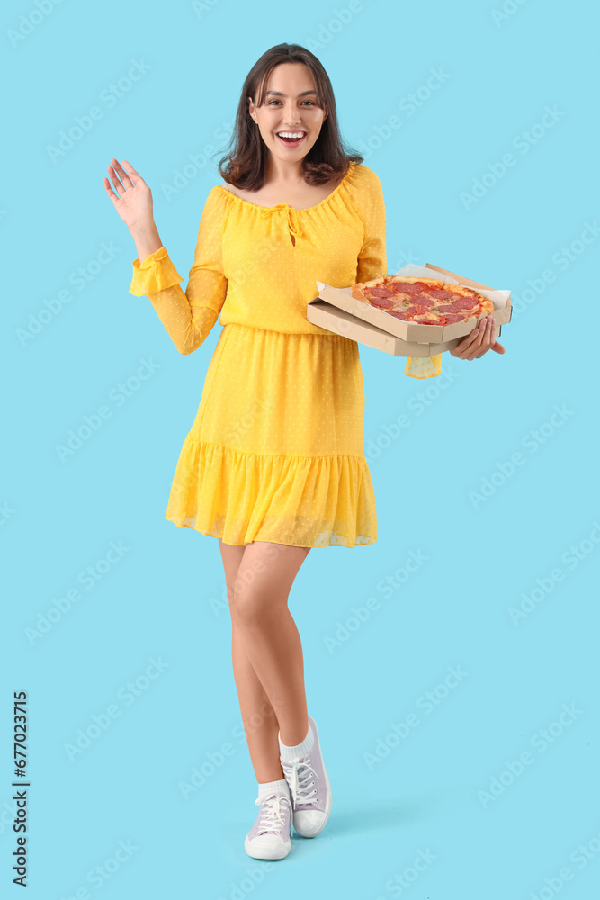 Young woman with tasty pepperoni pizza on blue background