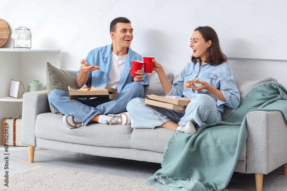 Young couple with drinks eating tasty pepperoni pizza at home