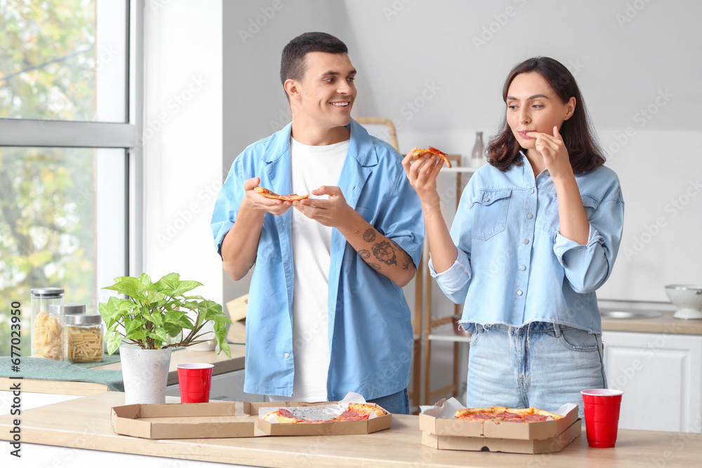 Young couple eating tasty pepperoni pizza in kitchen