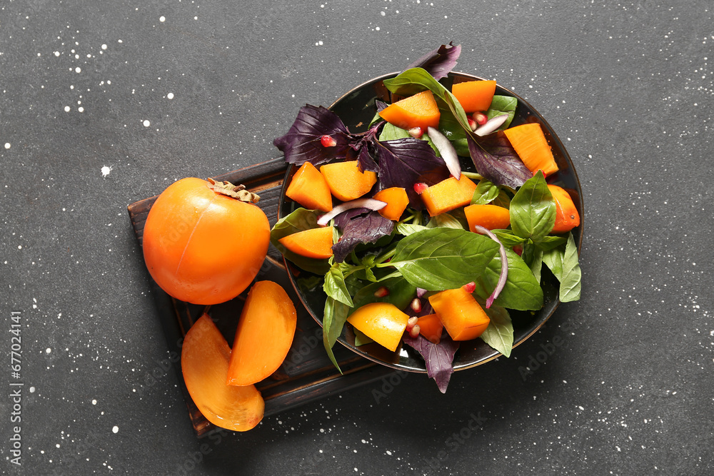 Bowl of delicious salad with persimmon, pomegranate seeds and onion on black background